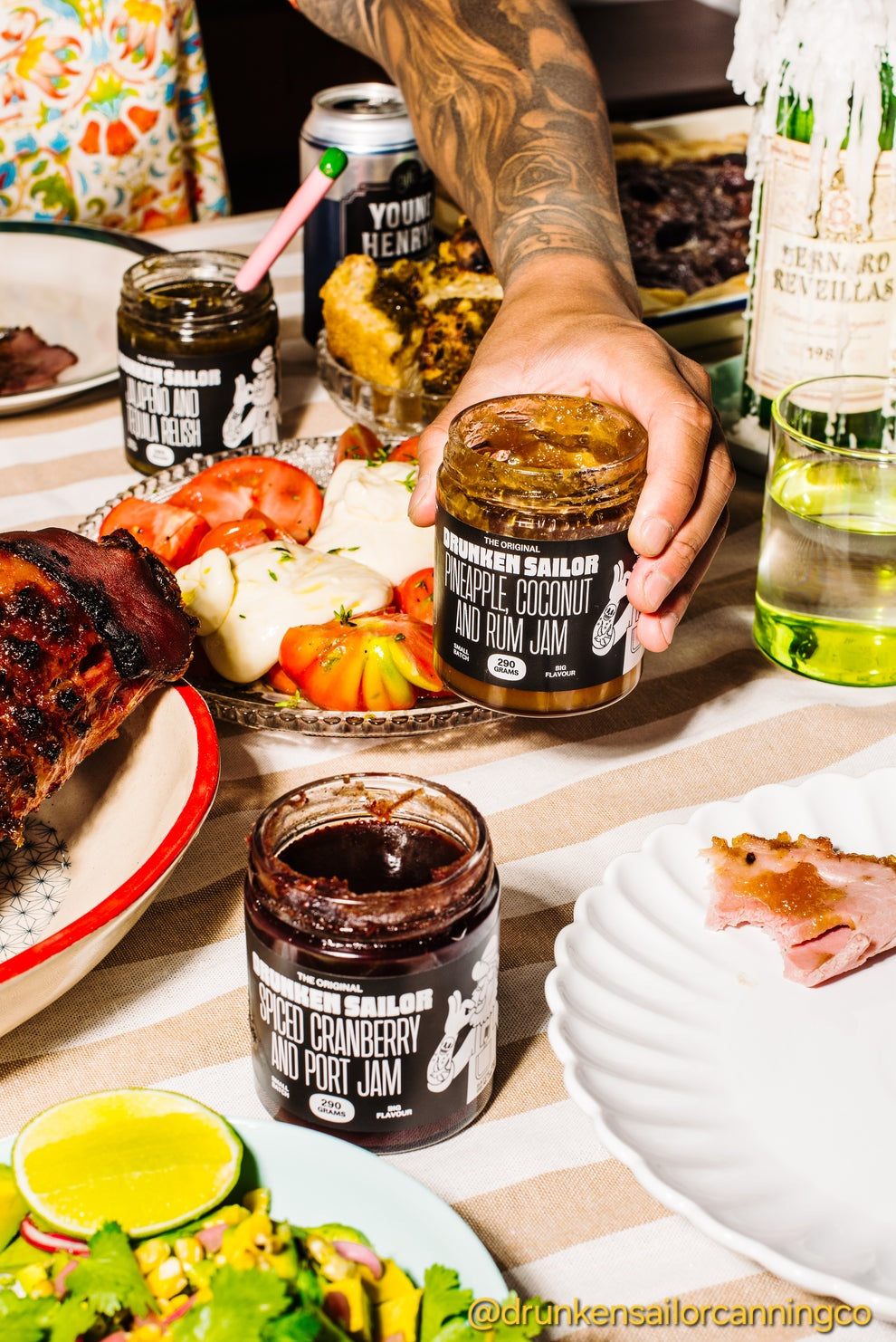 Person holding a jar of Drunken Sailor jam with a table full of food and drinks in the background.