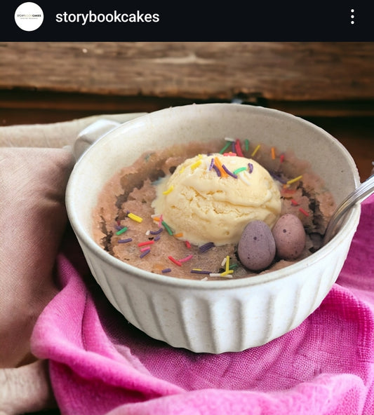 Mug cake with ice cream and sprinkles on top of pink and white fabric.
