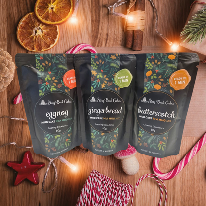 Three packs of Storybook Cakes mud cake mixes on a wooden surface with festive decorations.