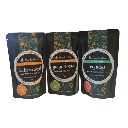 Three stand-up pouches of Story Book Cakes gluten-free mud cake in a mix, shown side by side on a white background. The pouches are labelled butterscotch, gingerbread, and eggnog, with dark green and black packaging featuring botanical illustrations and orange, green, and teal accents.