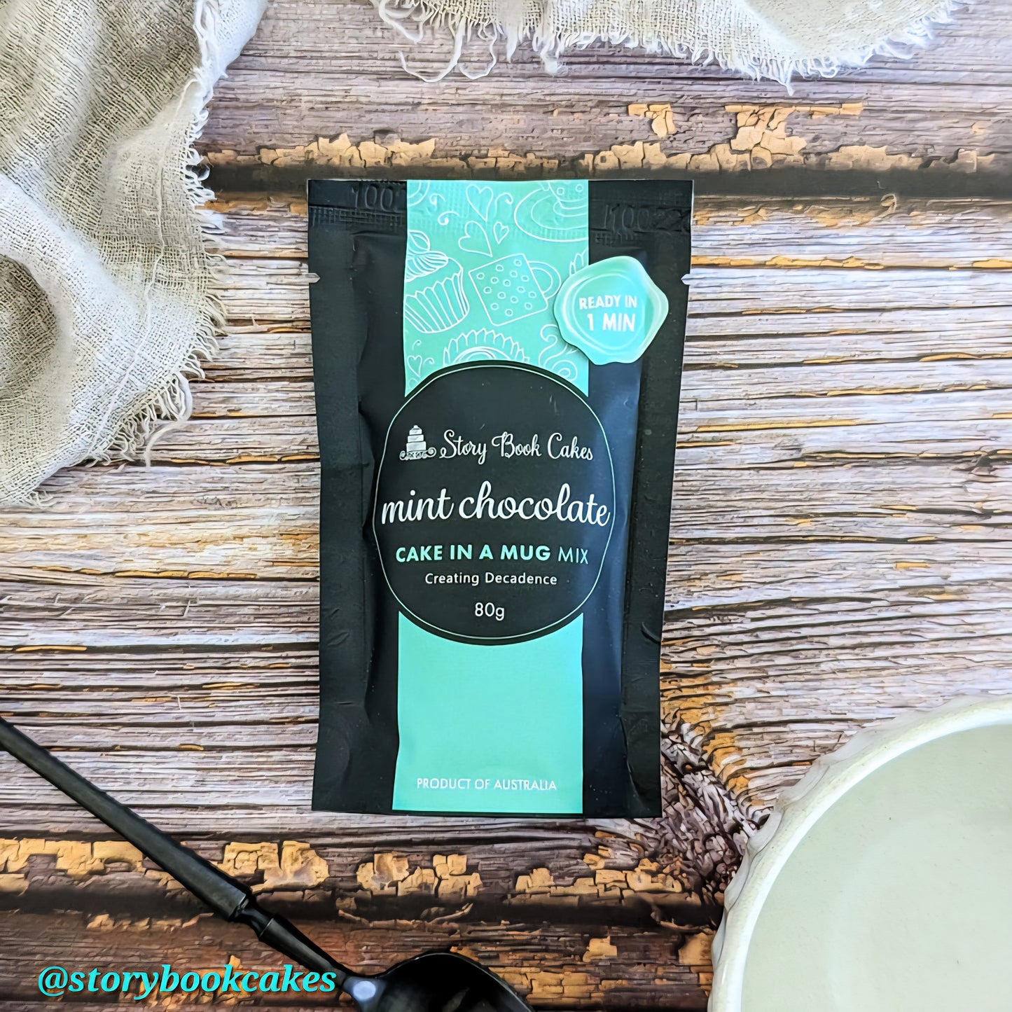 Packaged mint chocolate cake in a mug mix on a wooden surface with a bowl and spoon.