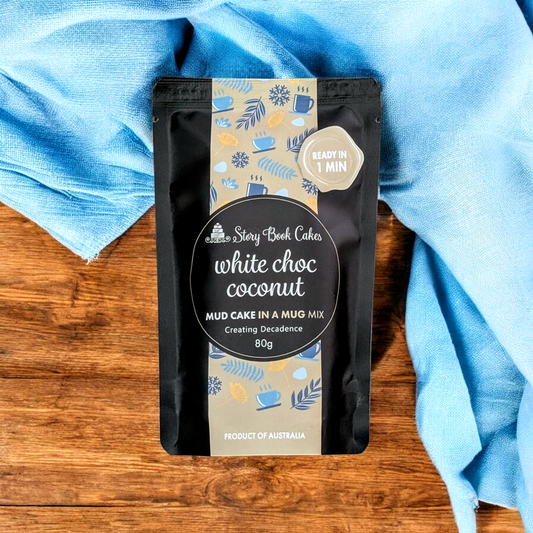 Packaged white choc coconut mud cake mix on a wooden surface with a blue cloth